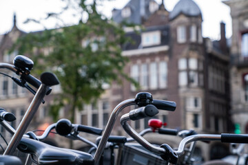 Obraz premium Close-up of bicycle handlebars and bells in a European city setting, with blurred historic architecture in the background, capturing the urban cycling culture and charm of European streets.