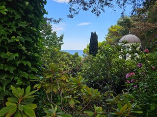 A stunning view of the sea from a lush secret garden with a romantic gazebo. Ideal for luxury travel, vacation concepts, or beautiful landscape design backgrounds.