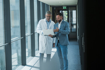 Doctor and businessman discussing work on notebook in office corridor