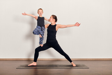 Young woman and child practice yoga together on mat. Both exhibit balance and focus, creating...