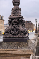 Obraz premium Close-up of an ornate, historic lamppost on the Pont Neuf bridge in Paris, France. The cast iron base features grotesque mascarons and sea creatures.