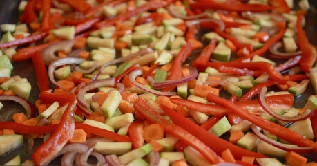 bunch of colorful fall vegetables—zucchini, red pepper, and carrots—arranged in a baking tray, drizzled with olive oil and herbs, ready to be roasted