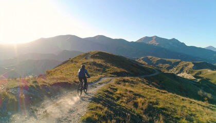 A cyclist rides a mountain bike along a dirt trail with scenic mountain views under a clear sky.