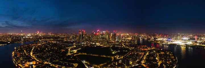 Naklejka premium Bright city lights illuminate London's skyline at night, showcasing iconic buildings and the River Thames winding through the city.