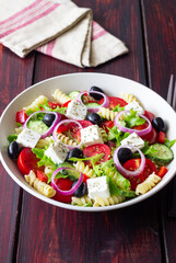 Greek pasta salad with feta cheese, tomatoes, onion, cucumbers, peppers and olives. Healthy eating. Vegetarian food.