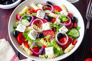 Greek pasta salad with feta cheese, tomatoes, onion, cucumbers, peppers and olives. Healthy eating. Vegetarian food.