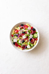 Greek pasta salad with feta cheese, tomatoes, onion, cucumbers, peppers and olives. Healthy eating. Vegetarian food.