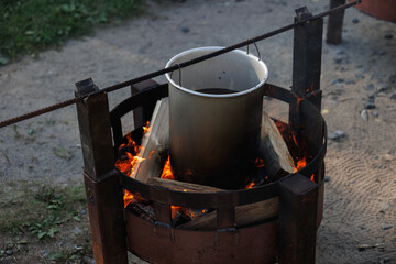 Setting up an outdoor cooking station with flames and a metal pot for boiling water