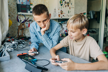 Two schoolboys play with computer tablets while sitting at a table in a children's room.