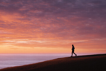 Silhouette of a man walking against a vibrant sunset over the ocean. Represents fitness, wellness, achievement, and new beginnings. Ideal for health, travel, or inspirational content.