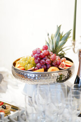 Metal bowl filled with grapes, figs, peaches and pineapple slices on banquet table.