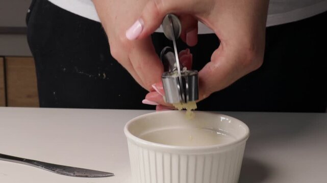 Crushing garlic with a garlic press in kitchen. Close-up of hands preparing fresh garlic cloves for cooking.