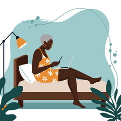 Senior Black woman comfortably working from home on her laptop and phone in bed. Depicts remote work, digital lifestyle, and flexibility.