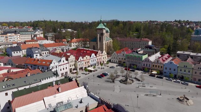 Drone view gliding past the historic Church of the Assumption of the Virgin Mary and colorful architecture lining Havlickovo Nam Square in Havlickuv Brod, Czechia.