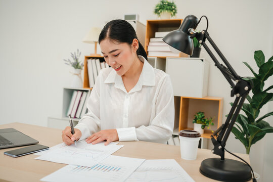 happy woman writing cocument or paperwork with laptop at home office