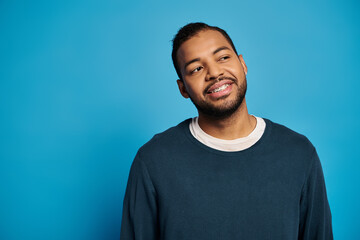 Young man in casual blue jumper smiles warmly in a studio with vibrant backdrop
