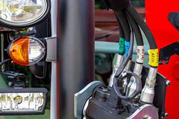 Close-up of headlights and hydraulic hoses marked with colorful labels on a modern agricultural tractor, detailed view of farming machinery components. © Adam