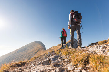 Obraz premium Mountaineer couple with backpacks and trekking poles doing a high mountain route on a nice sunny day. Seasonal vacation concept.