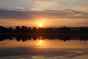 Beautiful moments of sunrise. Shot from the surface of the lake, the shore and trees against the beautiful sky. Morning fog. Reflection on the surface of the water.