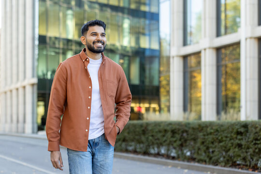 Young indian businessman walking near office building smiling and looking away