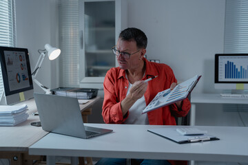 Mature businessman pointing at charts and graphs while having video conference with colleagues on laptop in modern office, explaining financial results and statistics