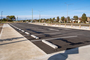 Empty asphalt parking lot in a suburban neighborhood of Australia, with marked bays, concrete wheel stops, and surrounding residential houses. Urban planning, public infrastructure, and transportation © Doublelee