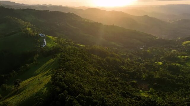 Aerial view of rolling green hills and valleys, dotted with buildings, bathed in the warm glow of the setting sun, Minas Gerais, Brazil.