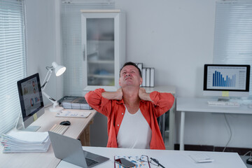 Office worker experiencing neck pain while sitting at desk with laptop, computer and paperwork,...