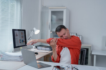 Office worker suffering from elbow pain while working on laptop, indicating potential health issues related to prolonged computer use and workplace ergonomics