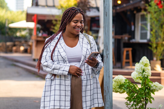 Plus size female with braids smiling while reading message on smartphone - Powered by Adobe