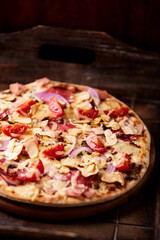 Pizza with ham, salami, cherry tomatoes and mozzarella cheese. Rustic wooden background. Soft focus. Close up.	