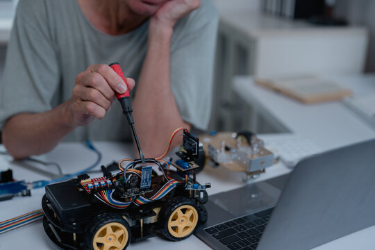 Robotics engineer assembling components of a robot car using a screwdriver and a laptop, focusing on innovation and technological development