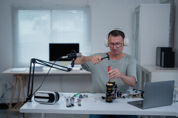 Electronics engineer wearing headphones, assembling robotics parts with a hammer and screwdriver, while recording a podcast in a modern office filled with technology and innovation