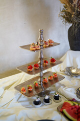 Tiered silver serving stand with assorted canapés arranged neatly on each level.
