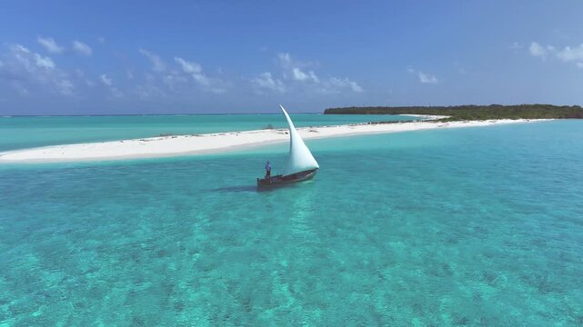Aerial view of a sailboat gliding across the turquoise waters towards a sandy island under a bright blue sky, Billefahi, Shaviyani Atoll, Maldives.