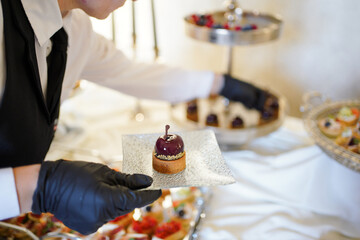 Waiter serving elegant dessert with glossy purple glaze on small tart.
