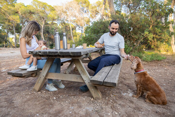 Candid family moment with mother breastfeeding and father feeding dog in the forest