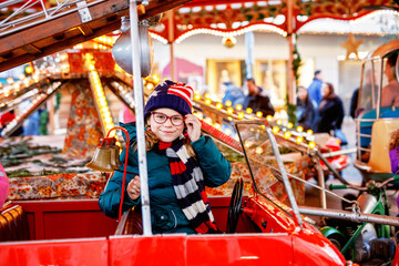 Obraz premium Little school girl riding on a merry go round carousel at Christmas funfair or market, outdoors. Happy child having fun on traditional family xmas market in Munich Germany