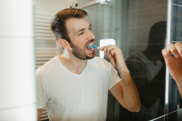 Young man brushing teeth in a modern bathroom. Morning hygiene routine, dental care and healthy lifestyle concept