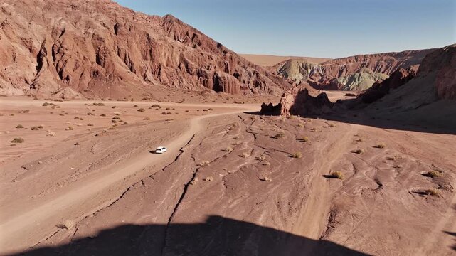 Aerial view of the stark Valle del Arcoiris, where a lone vehicle traverses the rugged terrain, showcasing the contrasting hues of the desert landscape, Chile.