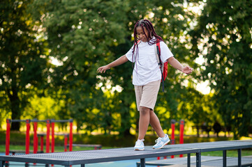 Girl with a red backpack walking on the log on a playground and keeping balance