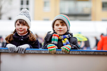 Two happy little kids girl and boy in colorful warm clothes skating on a rink of Christmas market...