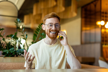 Red-haired in glasses smiling during phone call in cafe