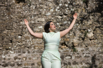 Young, beautiful, brunette woman in a white dress, arms open in thanksgiving and happiness, praying to god. Concept beauty, fashion, trendy, youth.