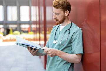 Man in green uniform leaning on wall with open patient records