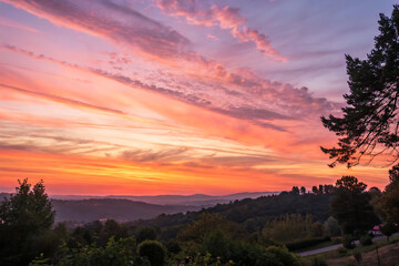 Obraz premium Sunset over the hills, a breathtaking view of a colorful sky with hues of orange, pink, and purple, creating a warm and inviting atmosphere over the landscape