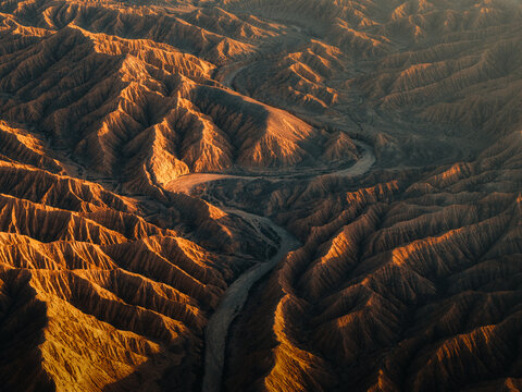 Aerial view of a river snaking through rugged, sun-baked canyons, the landscape painted in hues of ochre and deep shadow, Ak Say, Issyk-Kul Region, Kyrgyzstan.