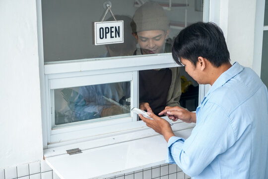 Young Asian Man Using Digital Tablet To Place Order At Service Window With Server Explain