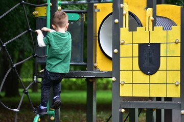 Young boy in green shirt climbing black rope net at playground. Child practicing strength, balance, and coordination while enjoying outdoor activity in park.