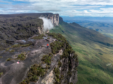 Aerial view of a tepui emerging majestically from the landscape, its dark rock contrasting with the vibrant green vegetation, capped with clouds, Roraima, Canaima, Venezuela.